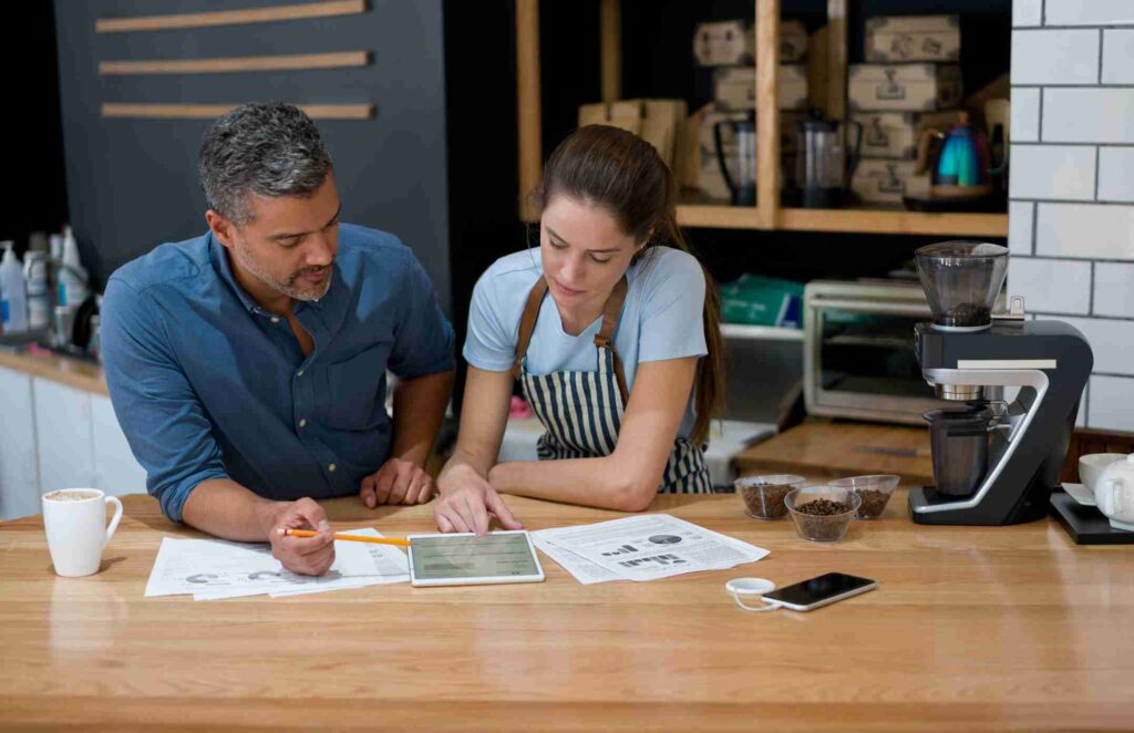 Two small business owners reviewing documents and a tablet together at a desk.